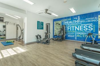 a gym with cardio machines and weights in a room with a wall with a quote